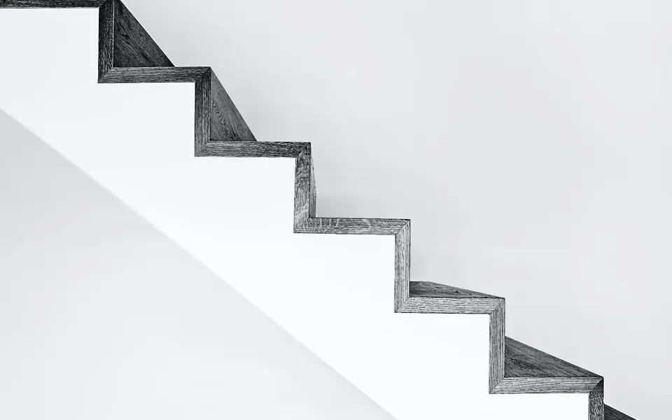 A dark timber staircase rising against a white wall